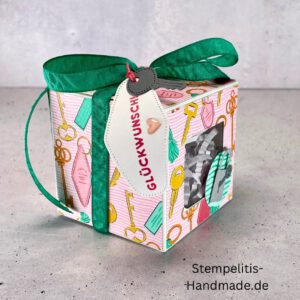 handdekorierte Fensterschachtel mit Glückwunsch-Anhänger, Geschenkbox mit Schlüsselmotiv und grünem Band, Nahaufnahme Fenster der Schachtel mit Füllung, runder Anhänger mit Schloss und Schlüssel, Schachtel geöffnet mit sichtbarem Inhalt, Glückwunsch-Tag an Geschenkbox, Geschenkverpackung für Einzug oder Prüfung